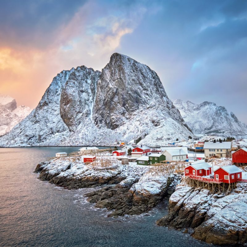 Famous tourist attraction Hamnoy fishing village on Lofoten Islands, Norway with red rorbu houses. With falling snow in winter on sunrise