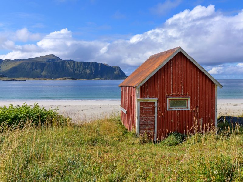 Sunny beach of Ramberg (Lofoten Island, Norway) with red wooden hut