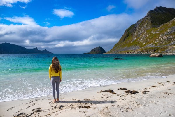 a beautiful long-haired girl enjoys the sunny weather on the famous paradise beach of haukland on the lofoten islands in northern norway; a beach walk in the norwegian fjords