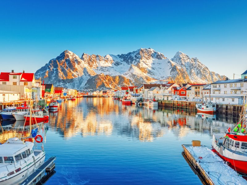 Beautiful Winter nature scene of fishing town on Lofoten Islands in Norway. Amazing sunny landscape of traditional houses rorbu and fishing boats in harbor.