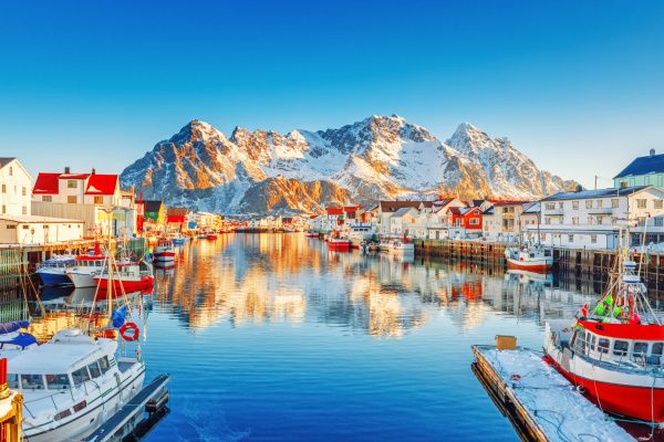 Beautiful Winter nature scene of fishing town on Lofoten Islands in Norway. Amazing sunny landscape of traditional houses rorbu and fishing boats in harbor.